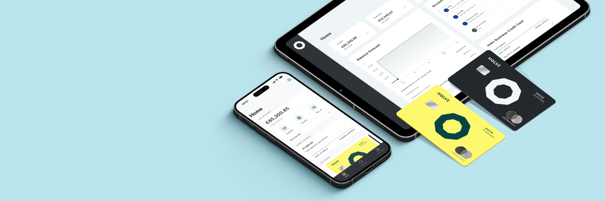 A phone lying next to a larger screen: both showcase the Holvi app in use. Two Holvi cards (debit and credit) lie next to them. The picture showcases the ease of having all your business finances in one place.